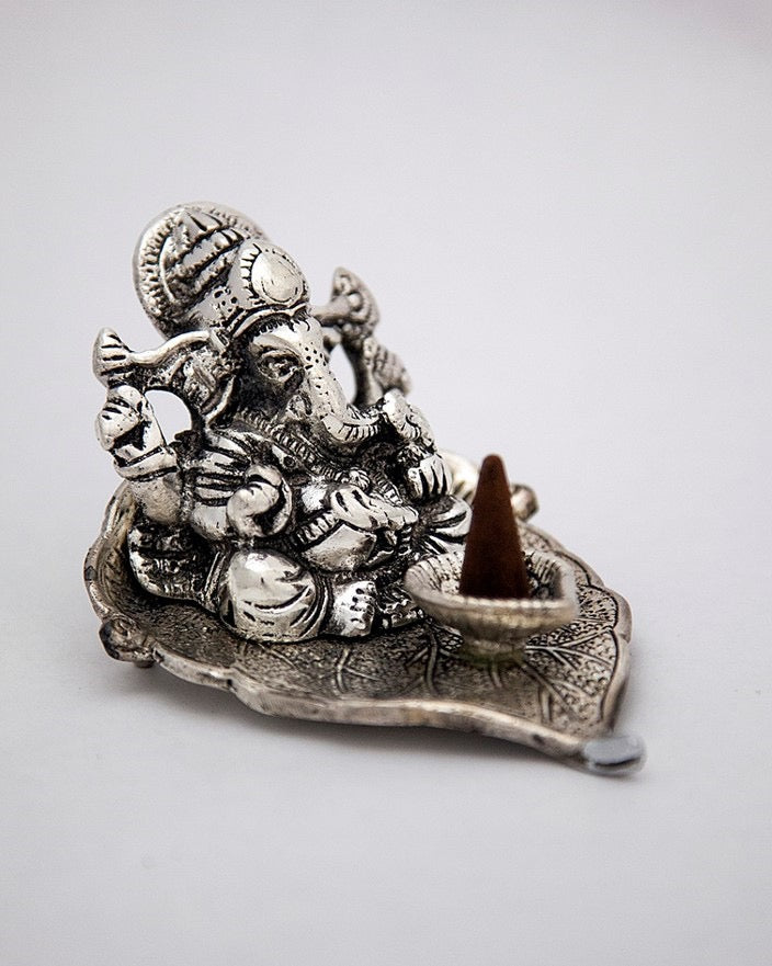 Silver deity figurine with an incense cone on a light gray background