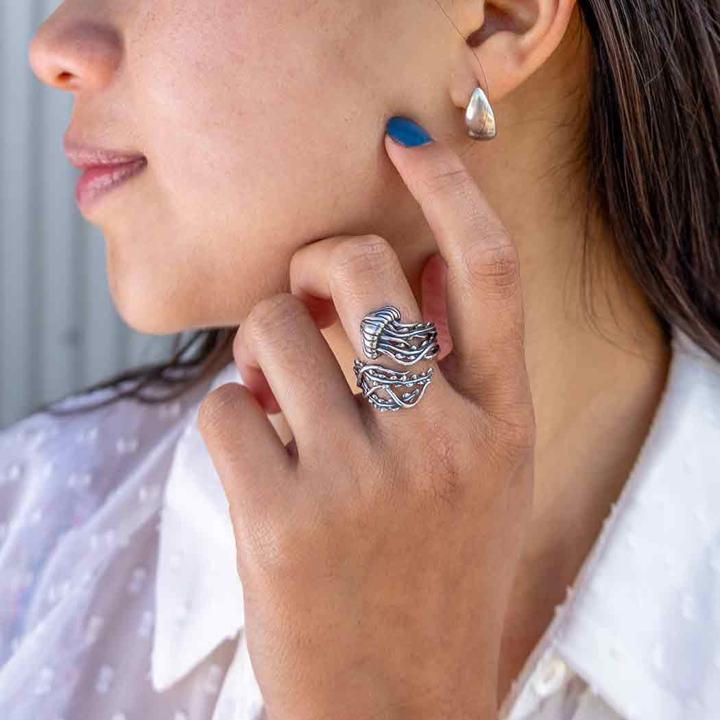 Close-up of a person wearing a silver ring and earrings, with a blurred background.