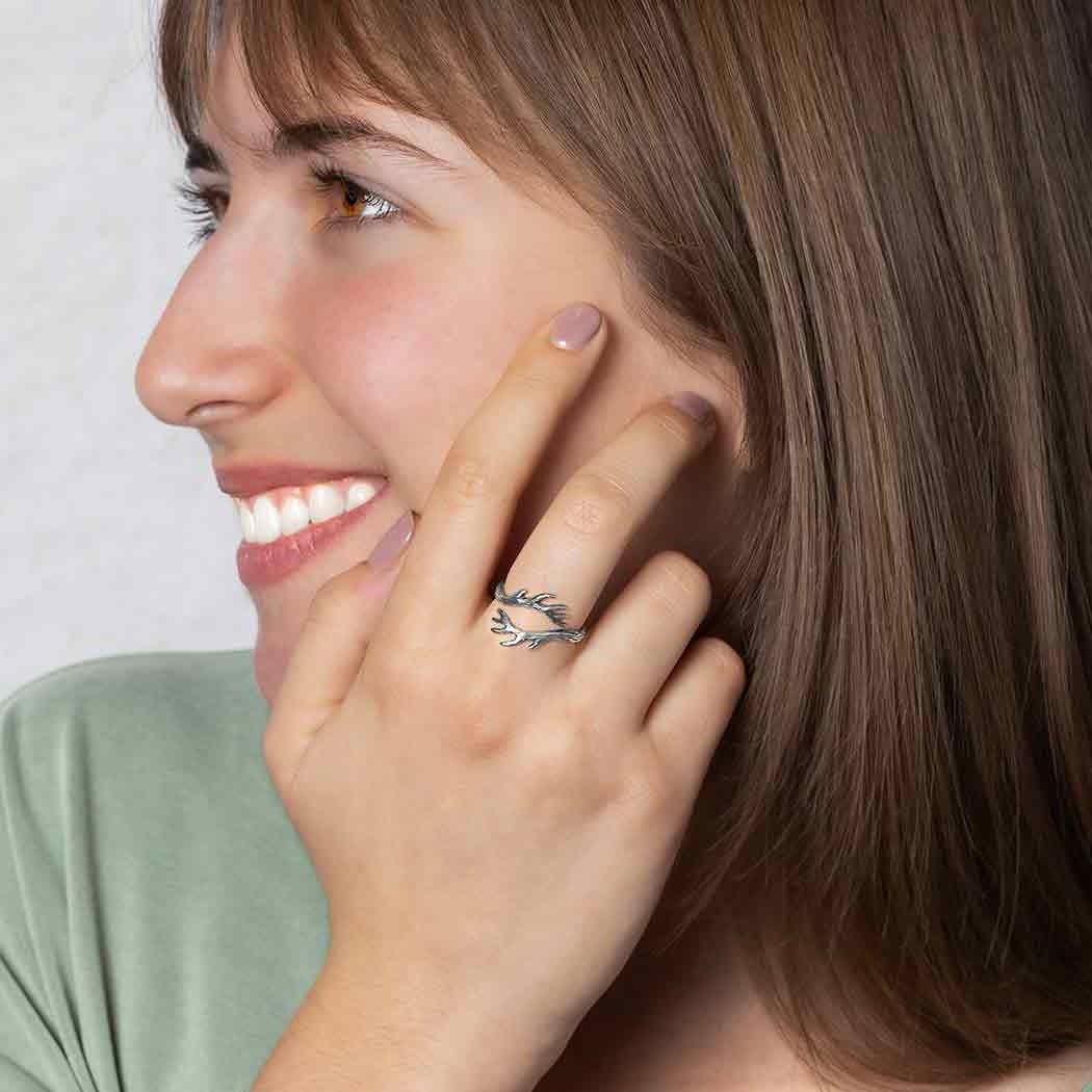 Woman wearing a silver ring on her finger, smiling and touching her ear.