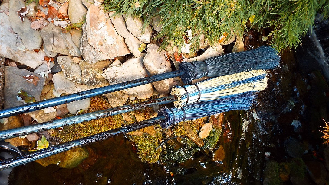 Two brooms leaning against a stone wall with greenery