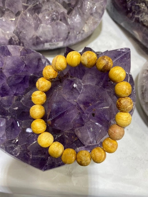 A beaded bracelet made of round, polished golden-yellow wooden beads, displayed on a purple amethyst crystal cluster.