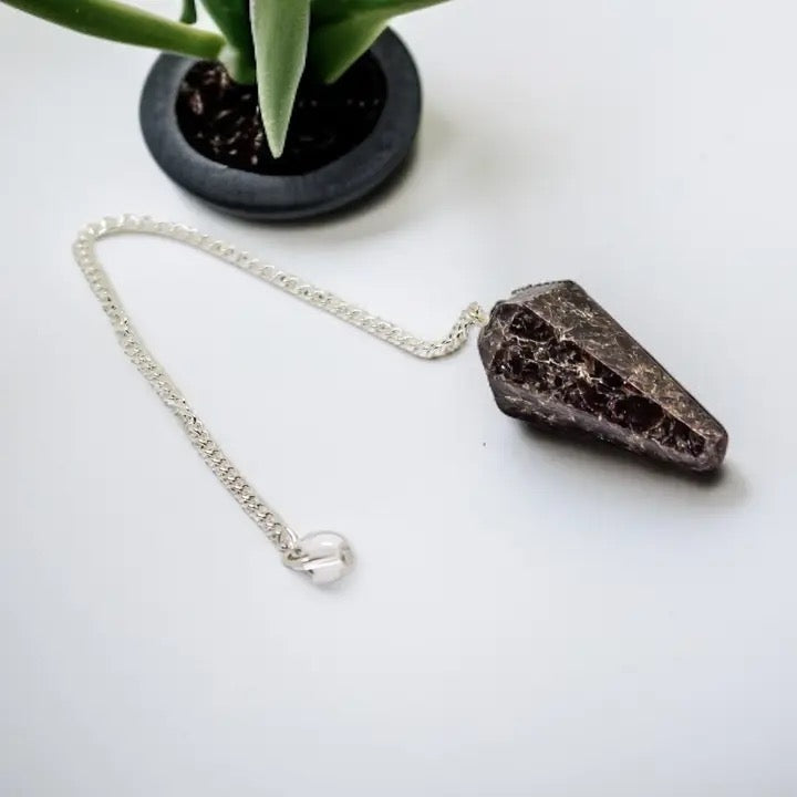 Pendulum Garnet on a white surface with a plant in the background