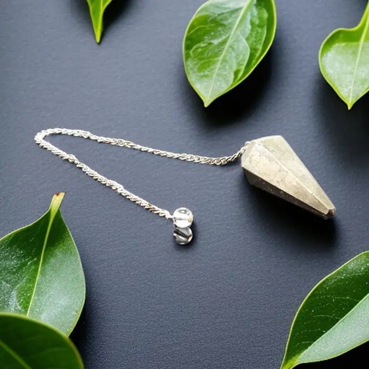 Pendulum with pyrite on a dark surface with green leaves