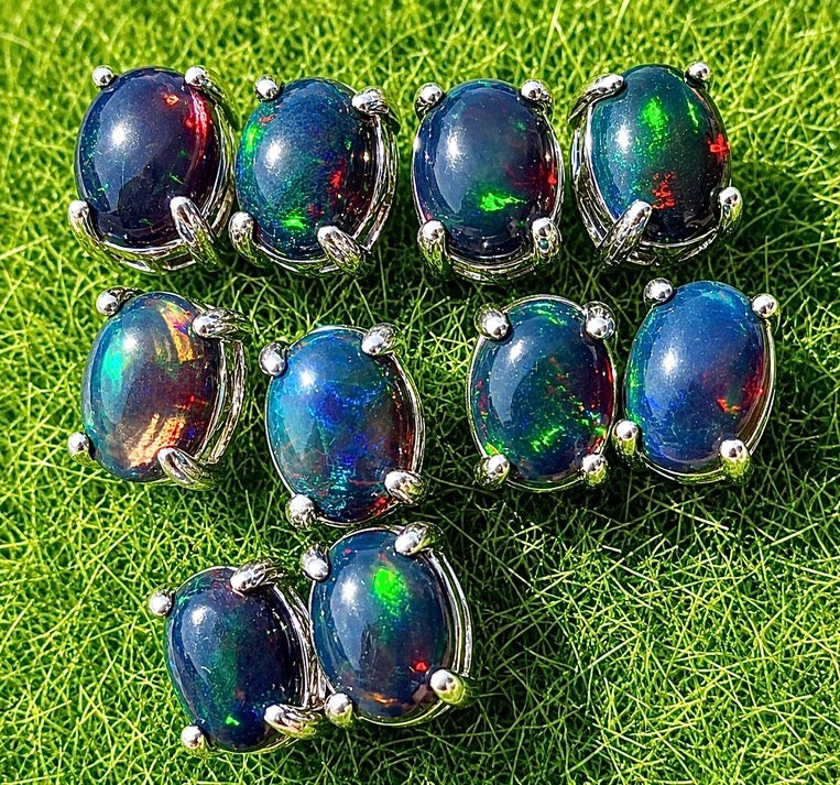 Nine oval opal gemstone jewelry pieces with silver prong settings arranged on a bright green grass-like textured background.
