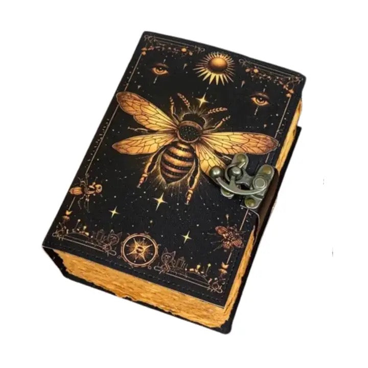 A black Leather journal with a metallic gold bee illustration, celestial motifs, and a small antique-style metal clasp on the front, shown on a plain white background.