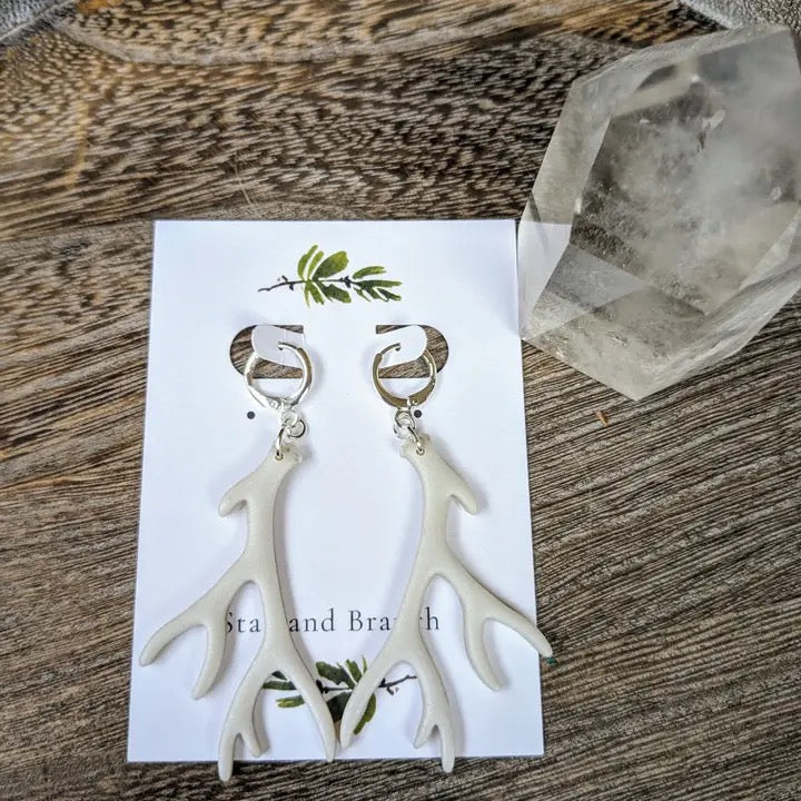 White antler-shaped earrings on a card with 'Star and Branch' branding, placed on a wooden surface.
