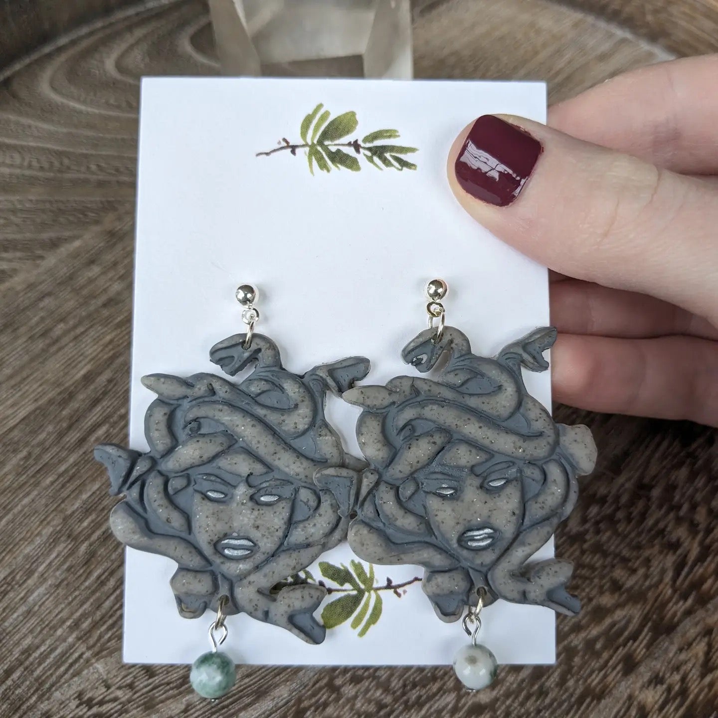 Pair of unique earrings on a card held by a hand with red nail polish.