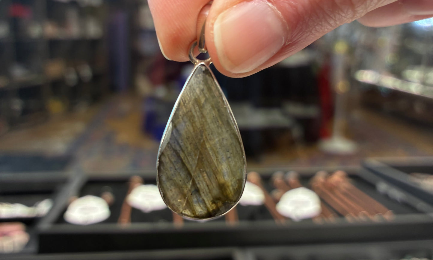 Teardrop-shaped pendant held by a hand with a blurred store background