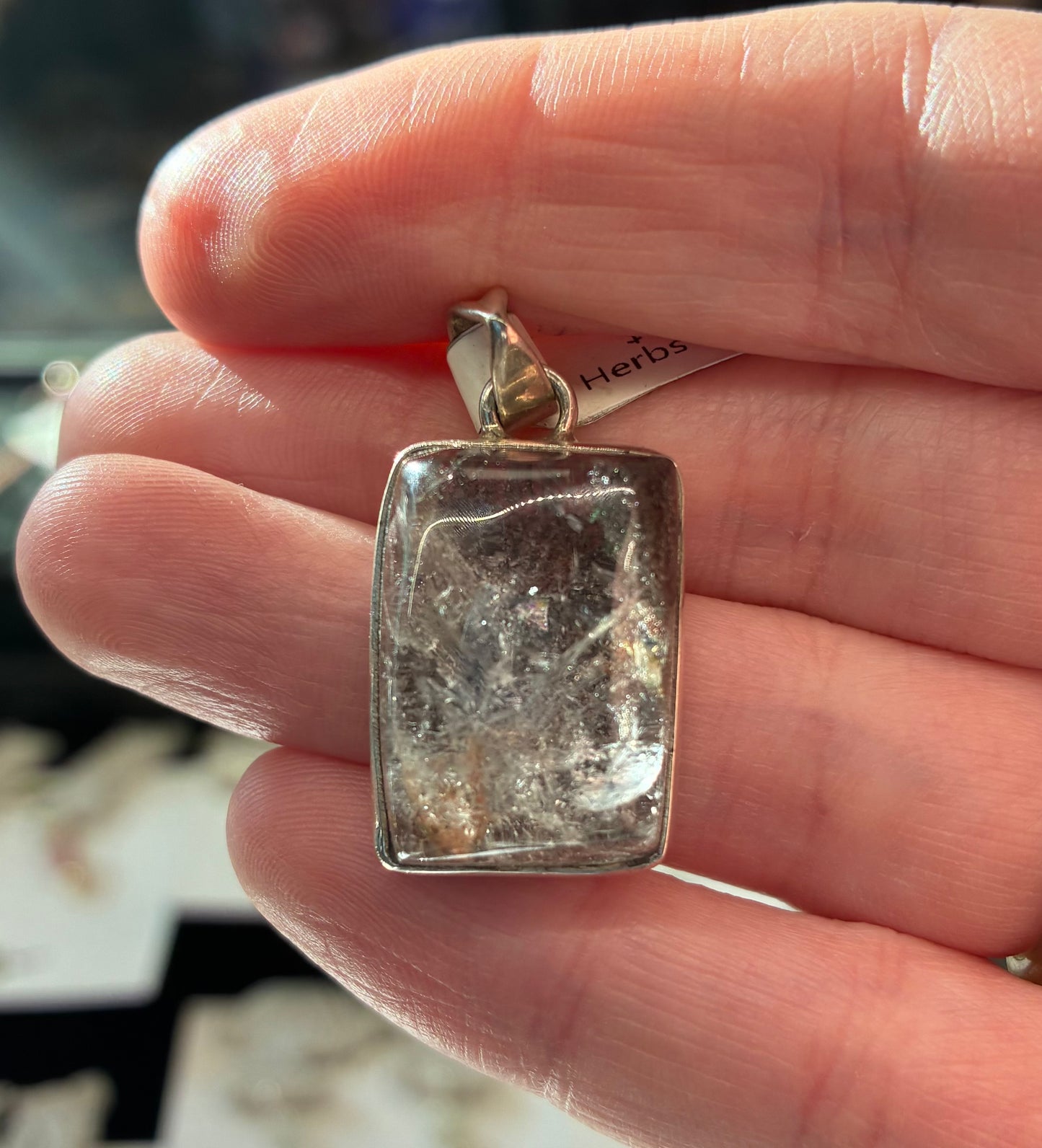 Hand holding a silver pendant with a textured surface