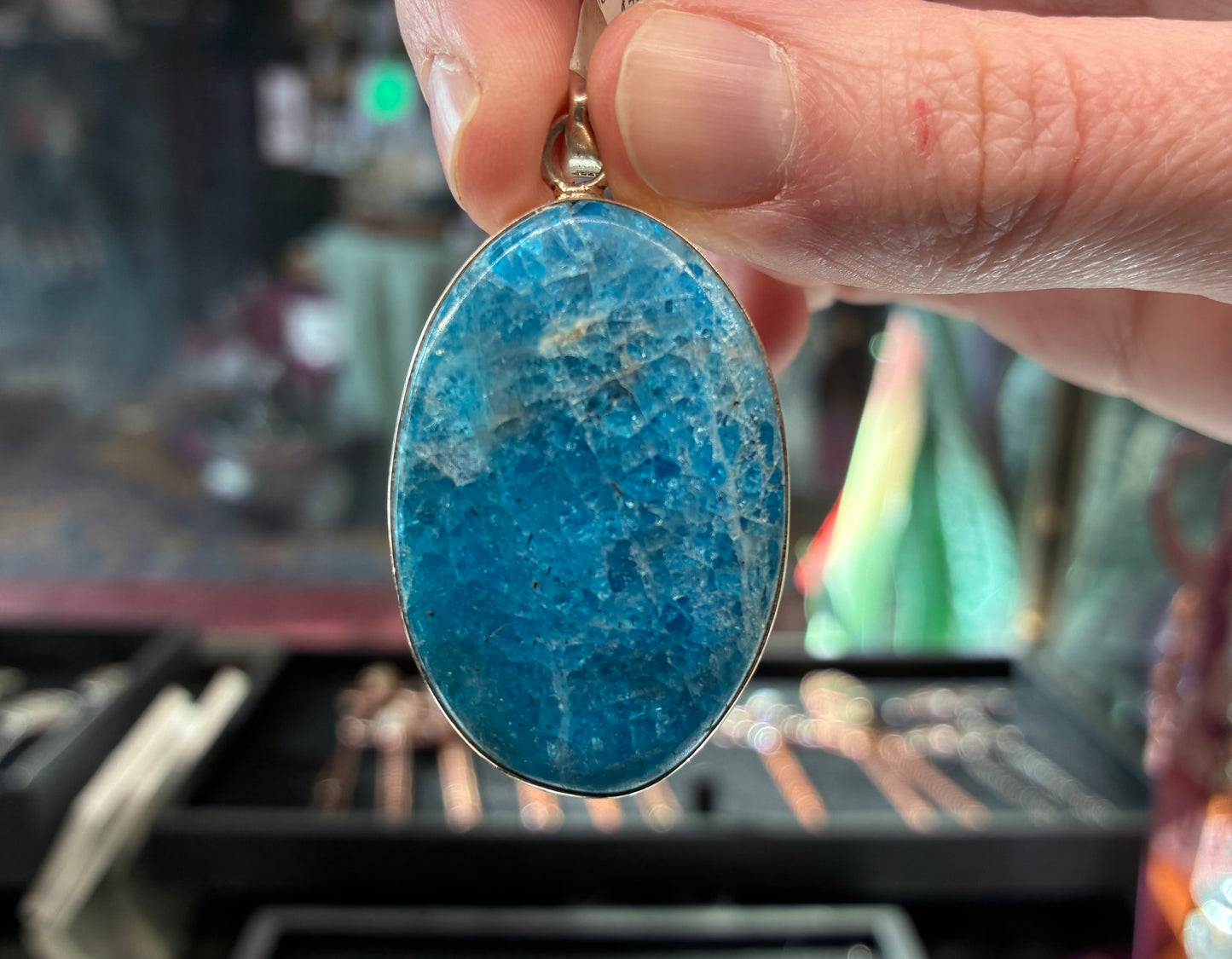 Blue stone pendant held by a hand with a blurred jewelry store background