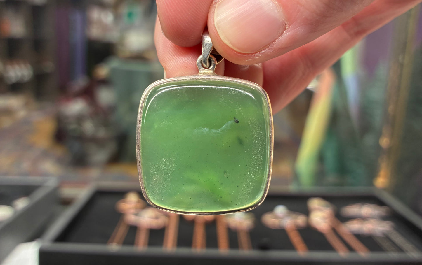 Green pendant held by a hand with a blurred background