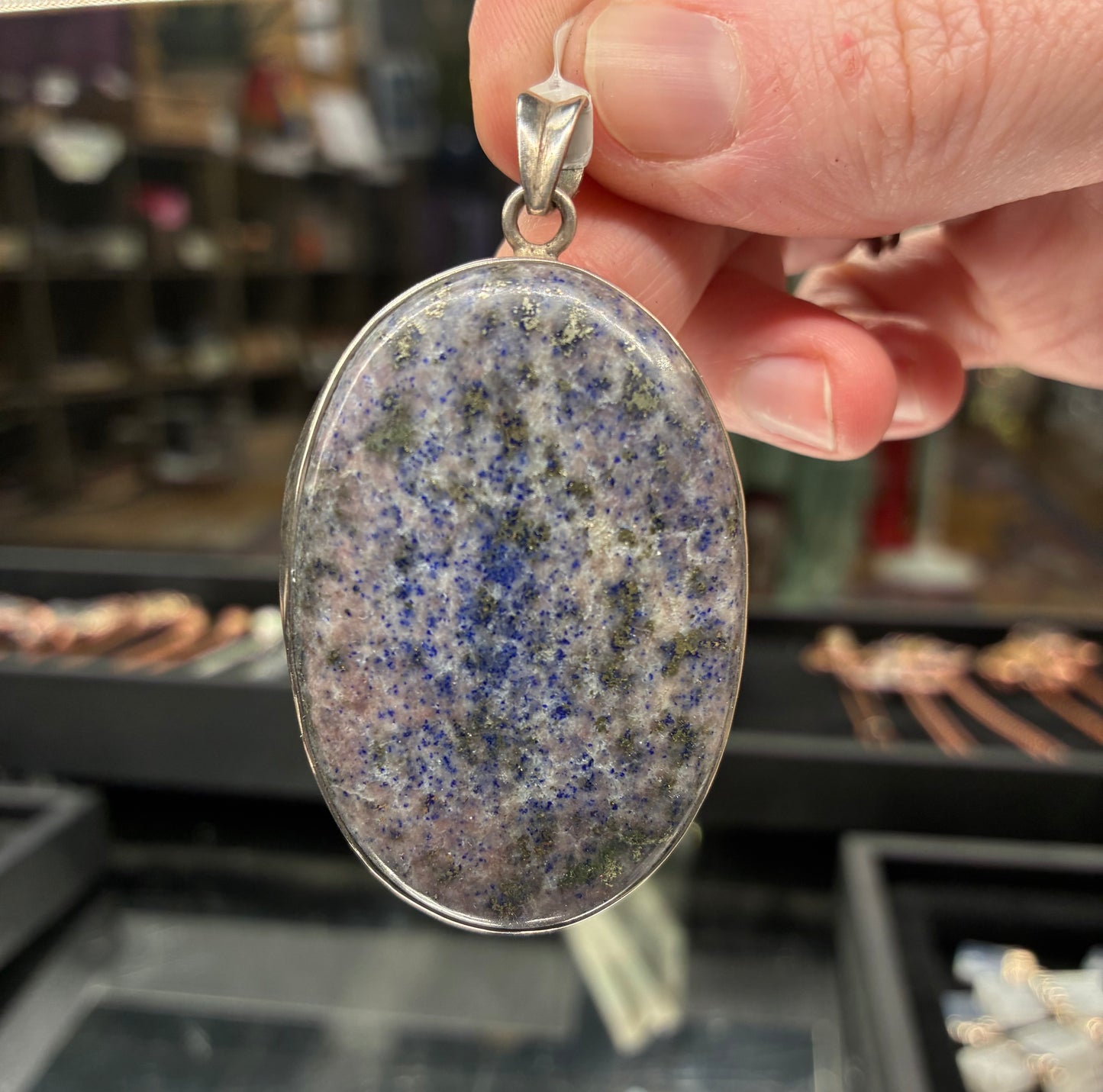 Oval-shaped pendant with speckled design held by a hand in a jewelry store.
