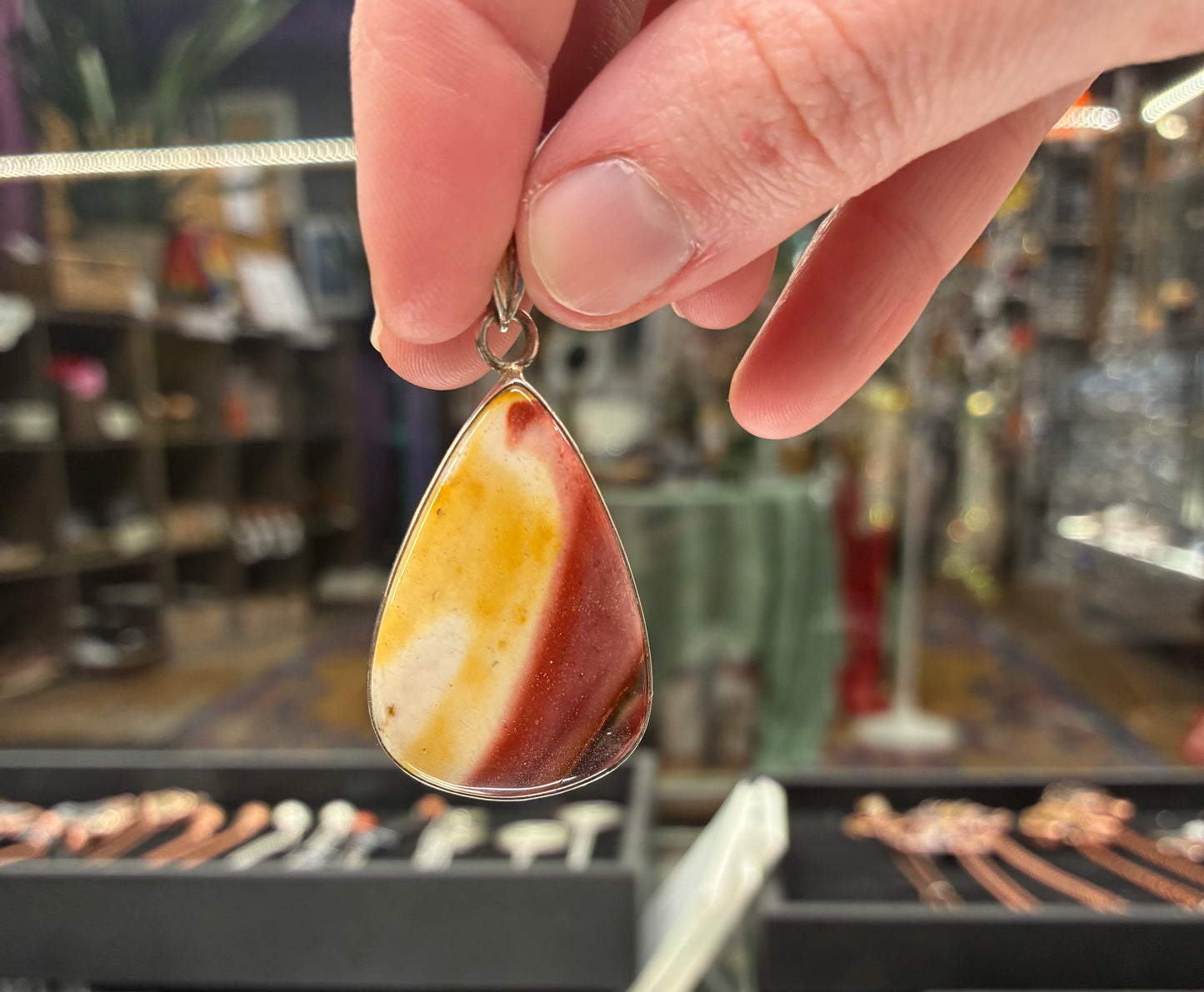 Teardrop-shaped pendant with a marbled design held by a hand in a jewelry store.