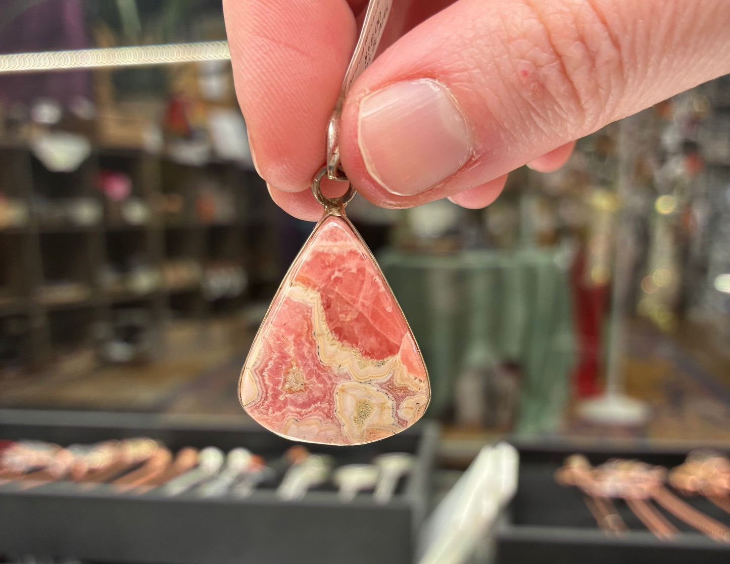 Hand holding a teardrop-shaped pendant with a pink and white marbled pattern against a blurred background.