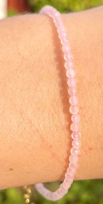 Close-up of a pink beaded bracelet on a wrist with a blurred green background