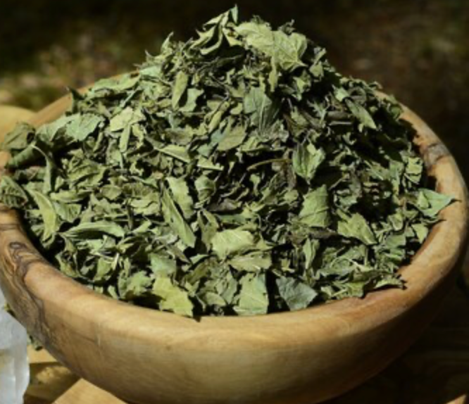 Wooden bowl filled with dried green herbs on a dark background