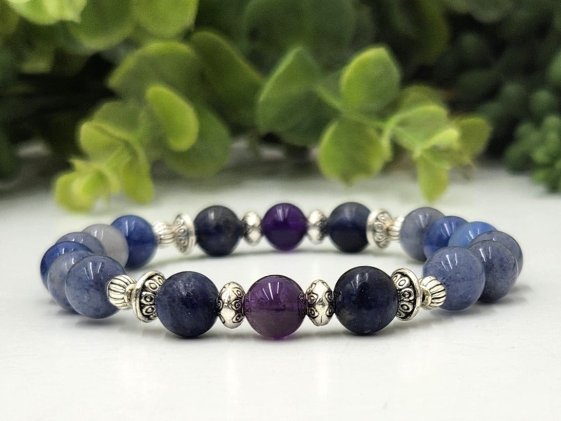 Beaded bracelet with blue and purple beads on a white surface with green leaves in the background
