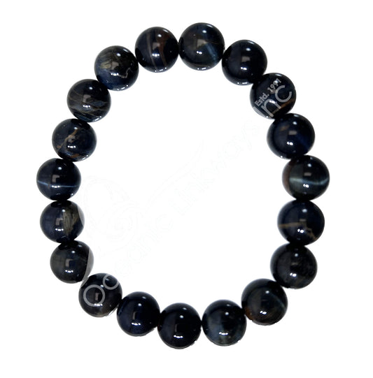A beaded stretch bracelet made of glossy, dark blue-gray round beads with natural banding, featuring a silver-toned metal charm engraved with 'BREATHE NC'.