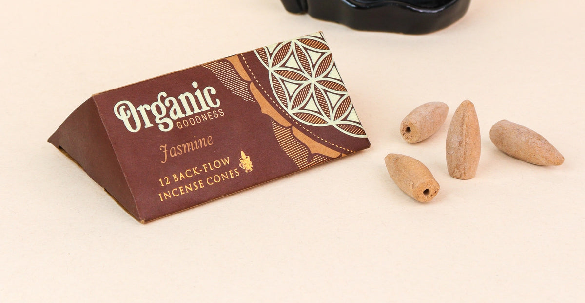 A triangular brown package labeled 'Organic Goddess Jasmine' with four small incense cones placed beside it on a light beige background.