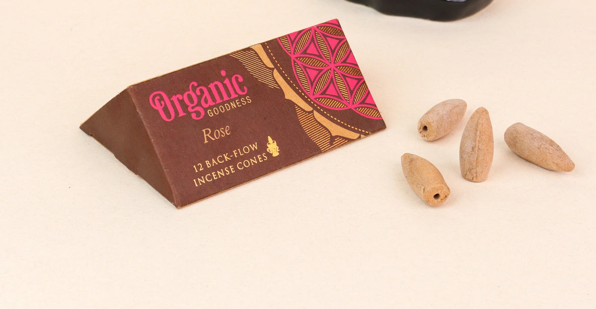 An organic rose incense cone package by Organic Goodness next to four light brown incense cones on a light beige background.