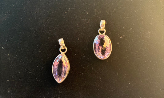Two silver pendants with purple stones on a black background