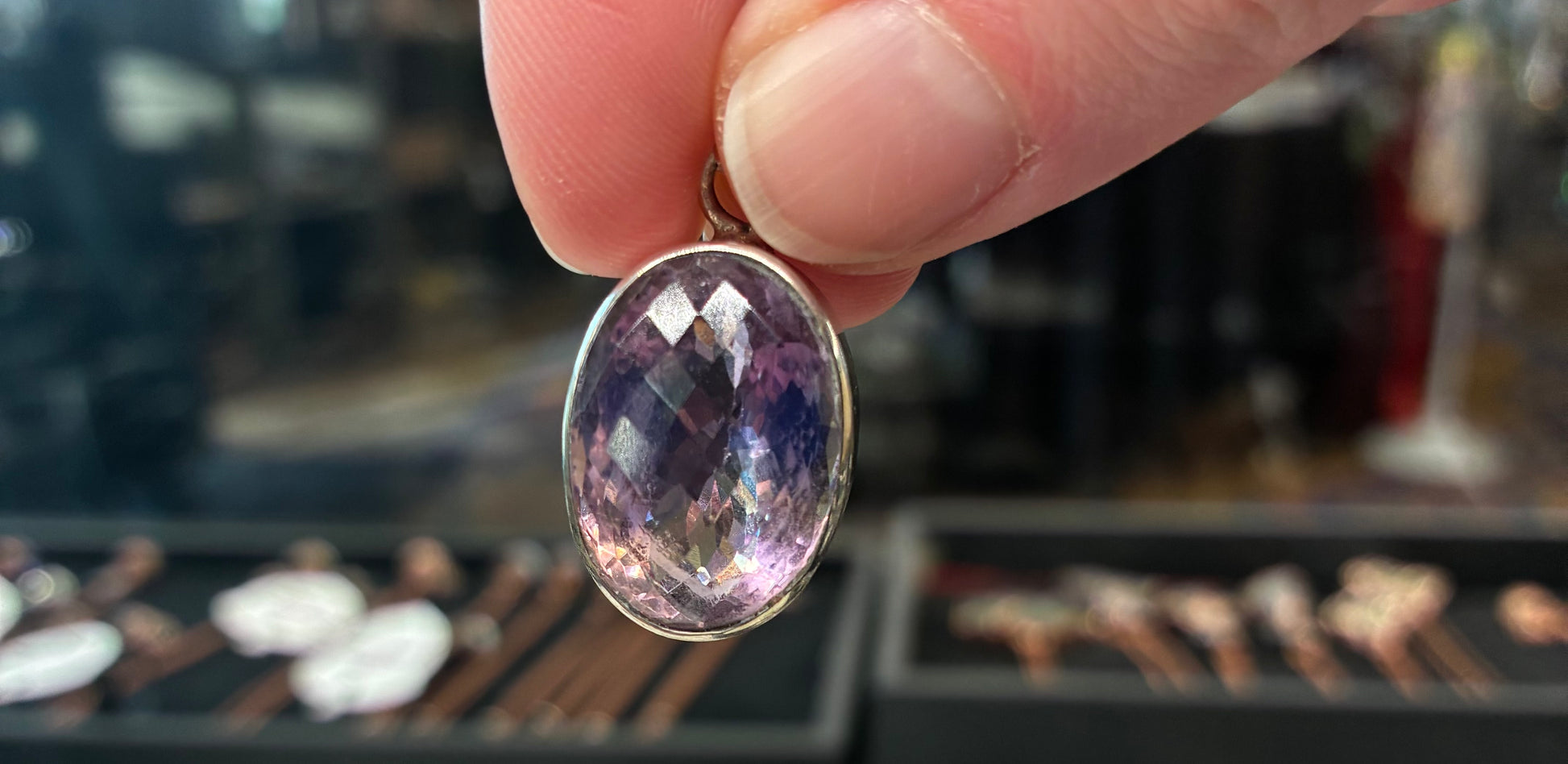 Hand holding a purple gemstone ring with a blurred jewelry store background