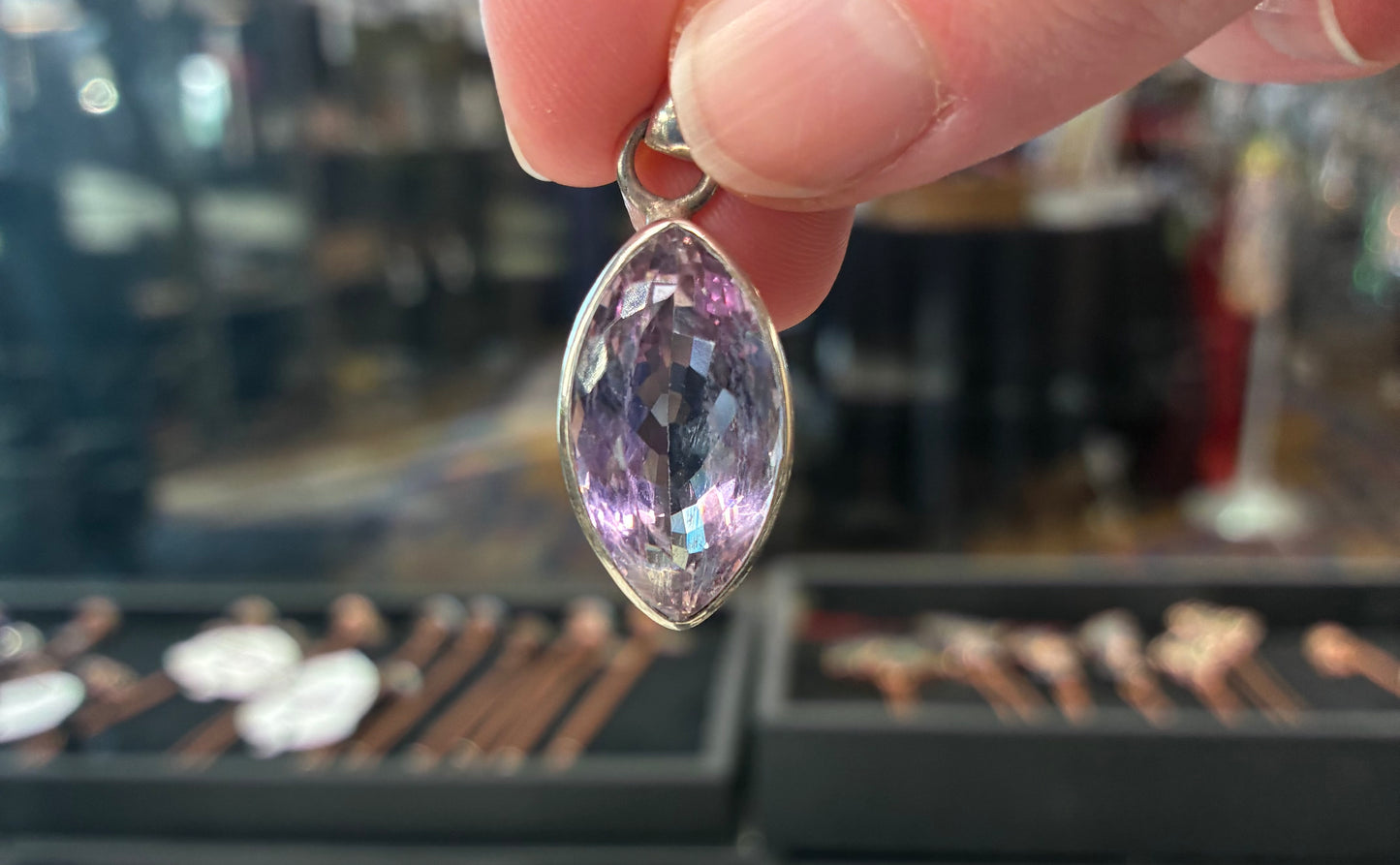 Hand holding a purple gemstone pendant with a blurred jewelry store background