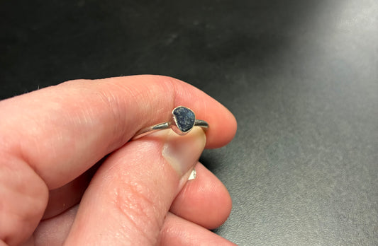Hand wearing a ring with a dark stone on a gray surface