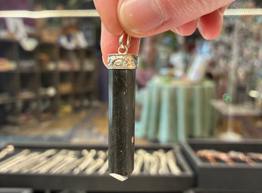 Hand holding a black cylindrical pendant with silver top against a blurred store background
