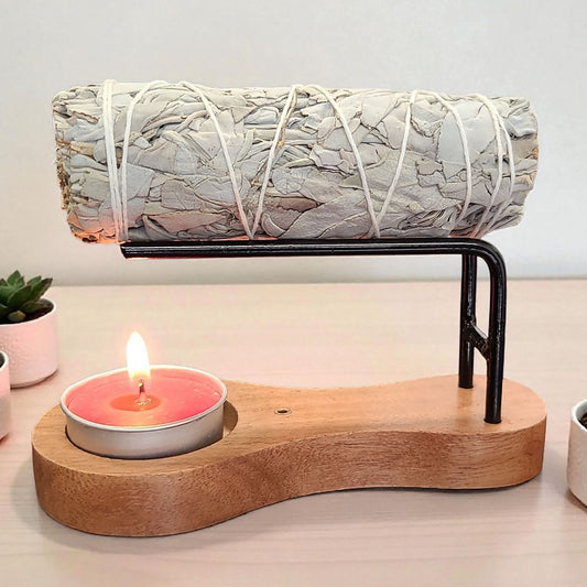 Sage smudge stick on a stand with a candle below on a wooden base.