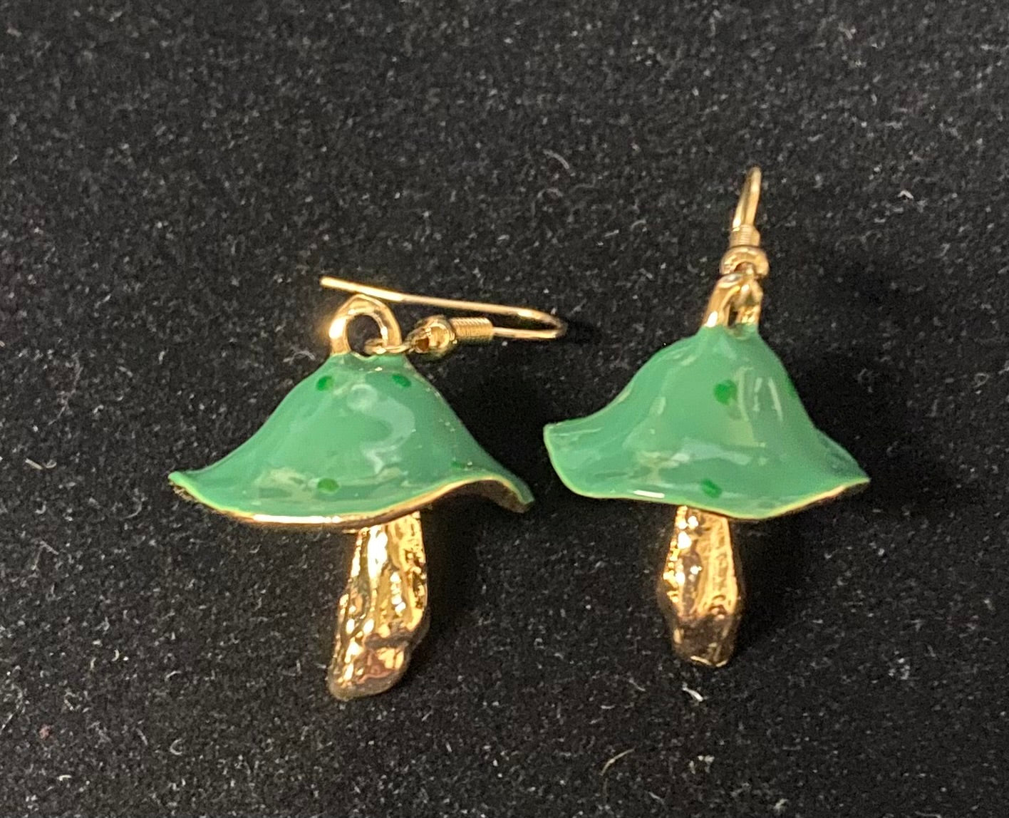A pair of mushroom-shaped earrings with glossy light green enamel caps and textured gold-tone stems and hooks, displayed on a black textured background.
