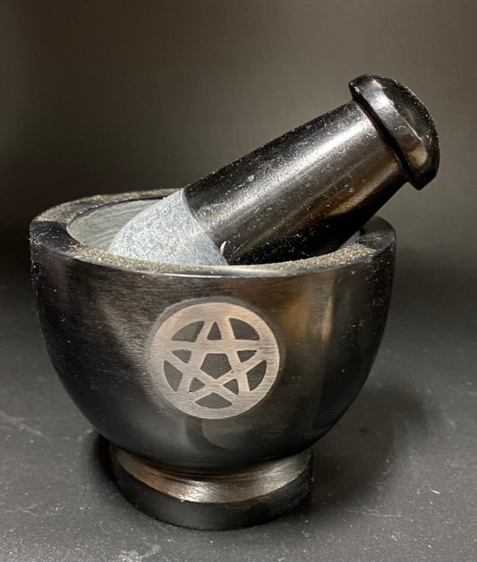A black stone mortar and pestle set with a silver pentagram symbol engraved on the side, photographed on a dark gray background.