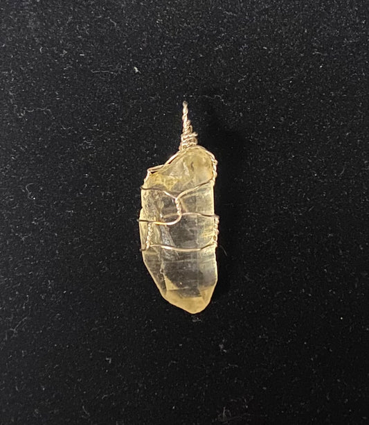 A small raw, irregular translucent crystal pendant wrapped with thin silver wire, shown against a black background.