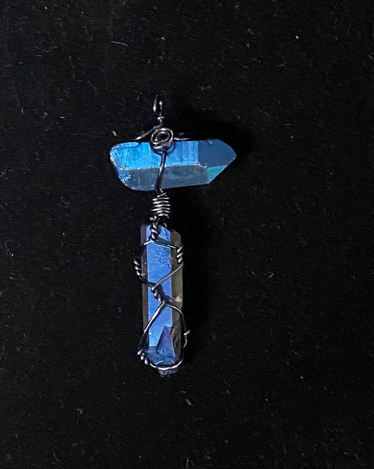 A handmade pendant featuring a blue titanium quartz point wrapped in black copper wire, hanging from a blue titanium quartz crystal, set against a black background.