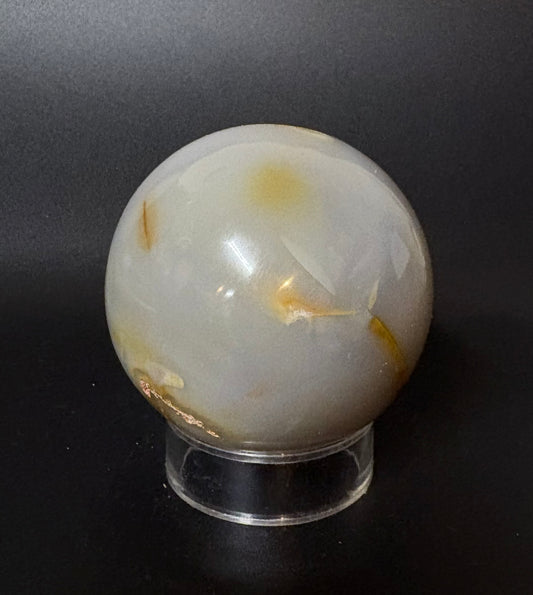 Blue Chalcedony sphere with gold inclusions on a clear stand against a black background