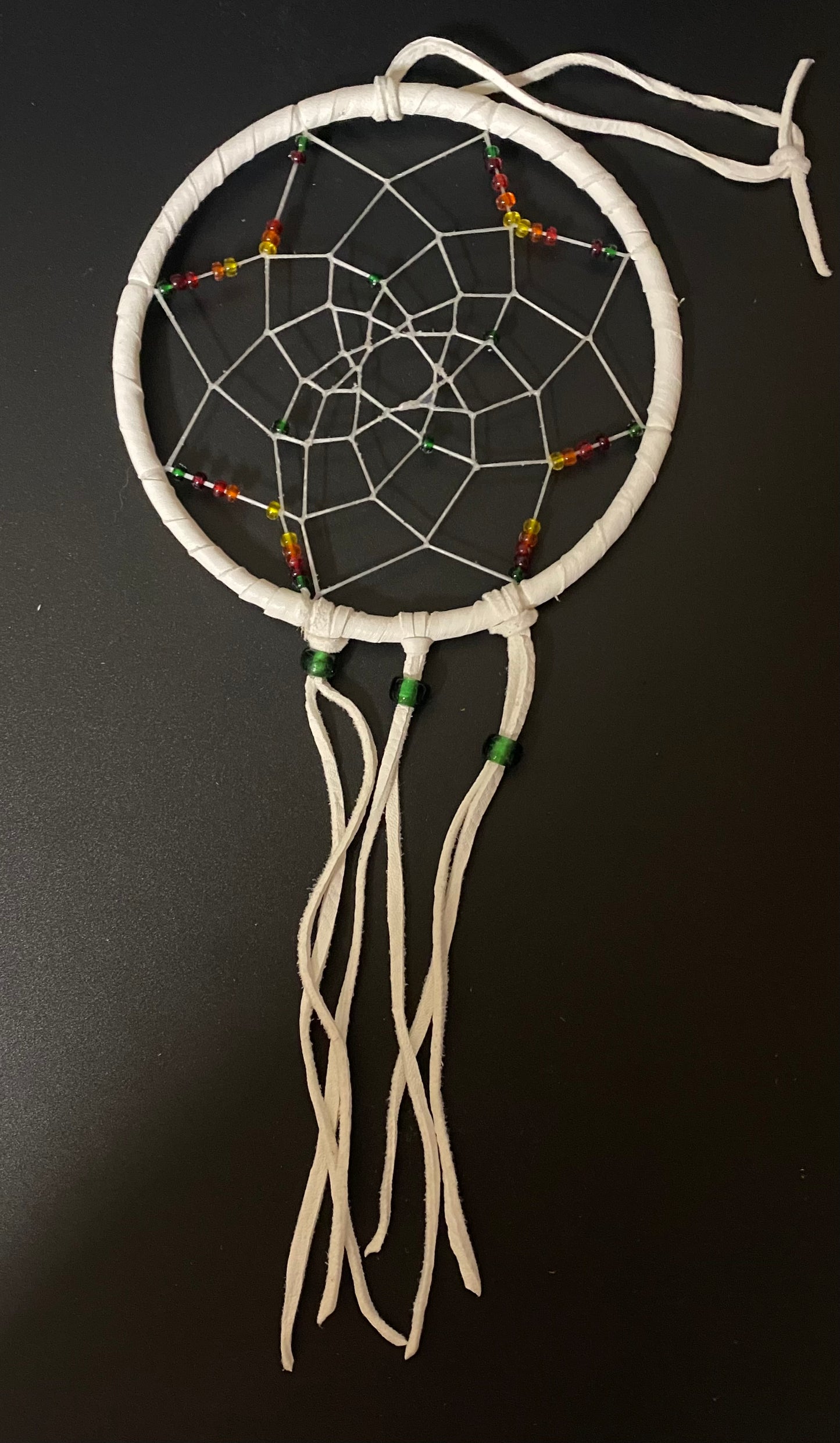 A white dreamcatcher with a circular hoop, white webbing, and small multicolored beads, photographed against a dark background.