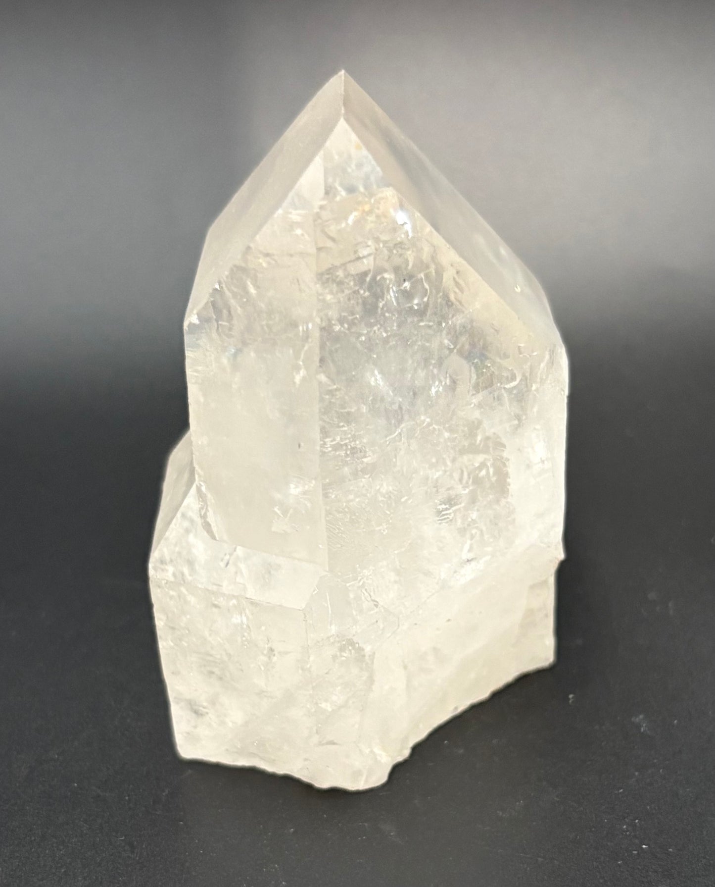 A polished quartz crystal with a pointed geometric shape, made of semi-translucent off-white material, photographed on a dark gray background.
