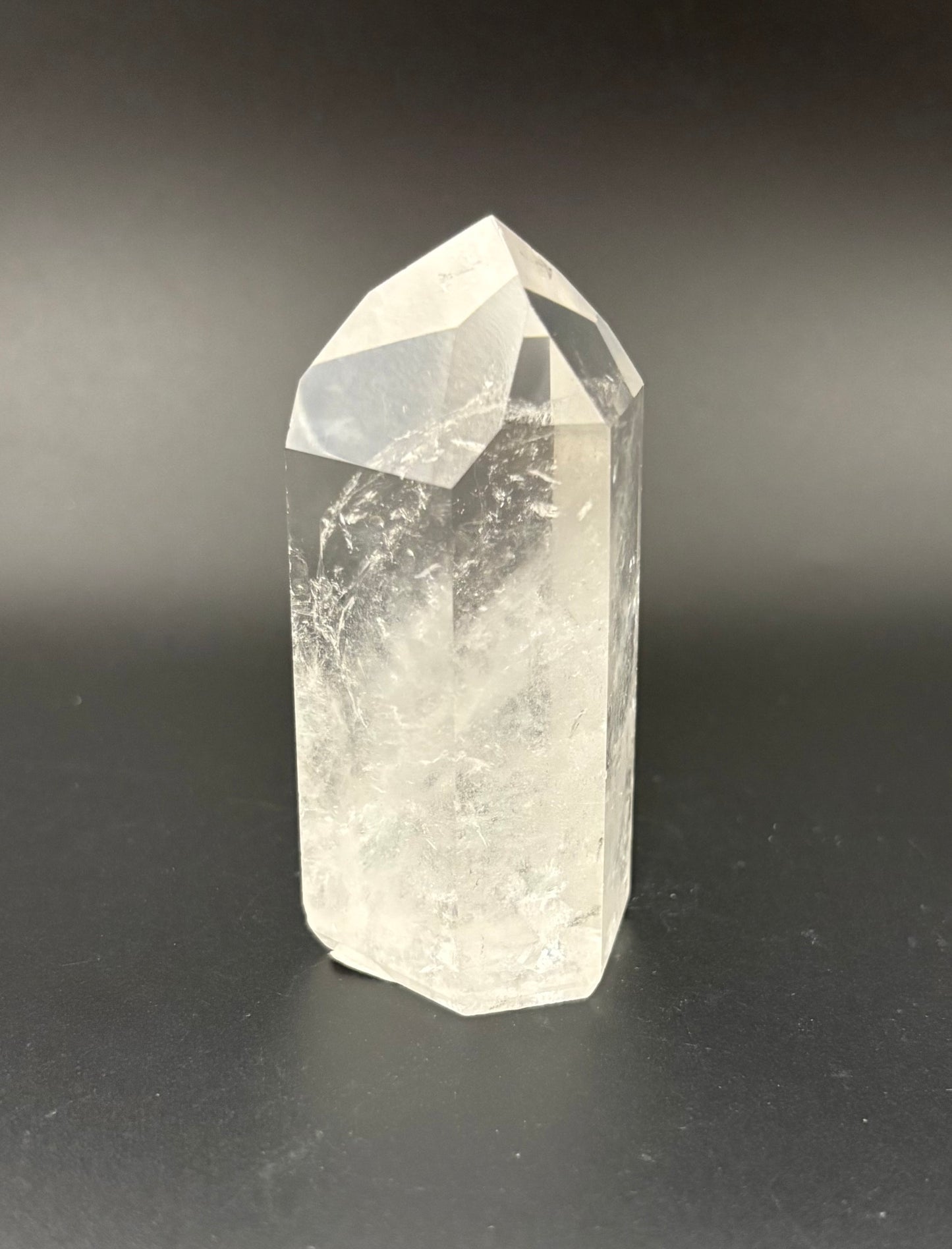 A natural clear quartz crystal point tower with internal inclusions, standing on a dark gray gradient background.
