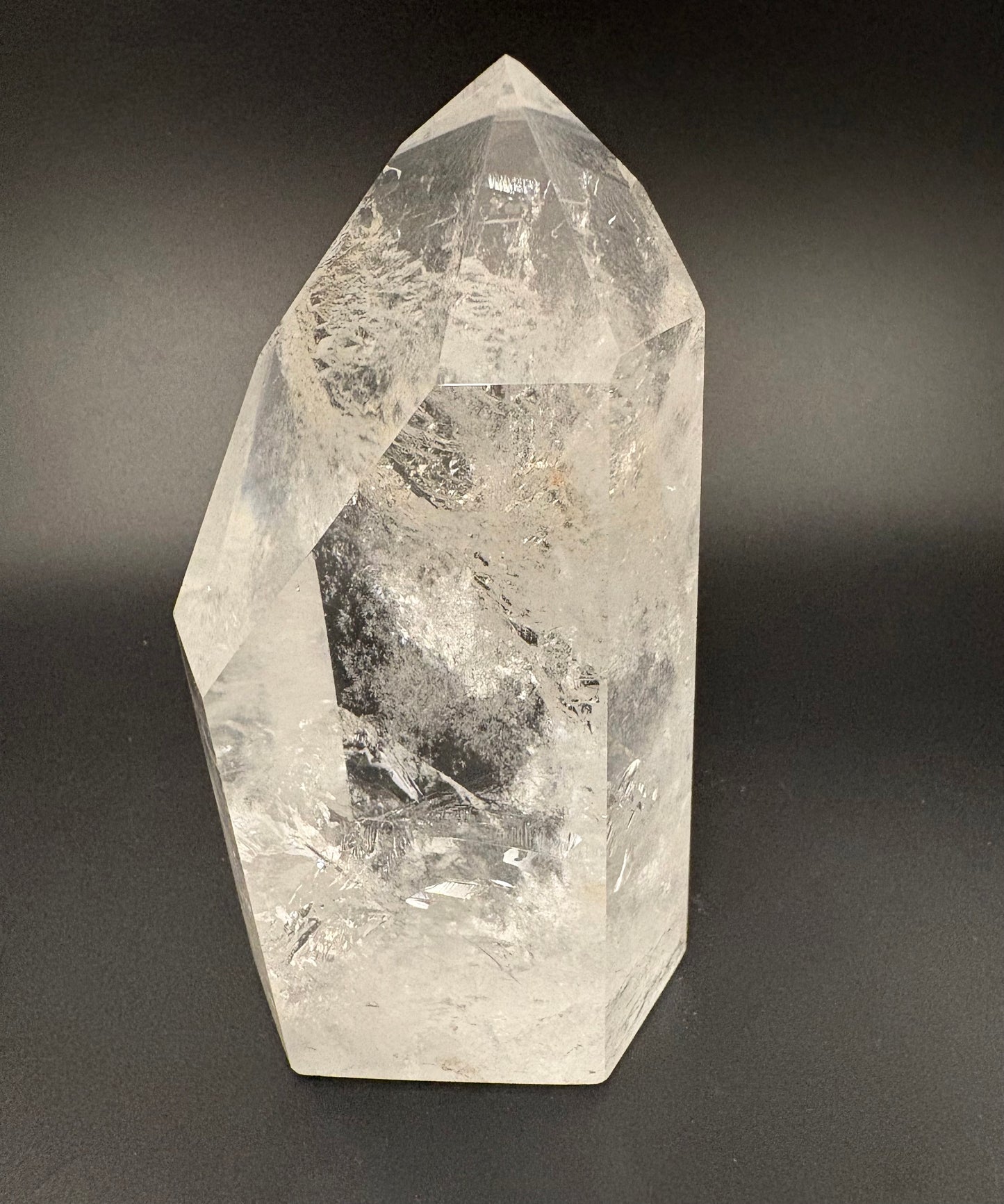 A natural clear quartz crystal point with internal inclusions, photographed against a dark gray gradient background.