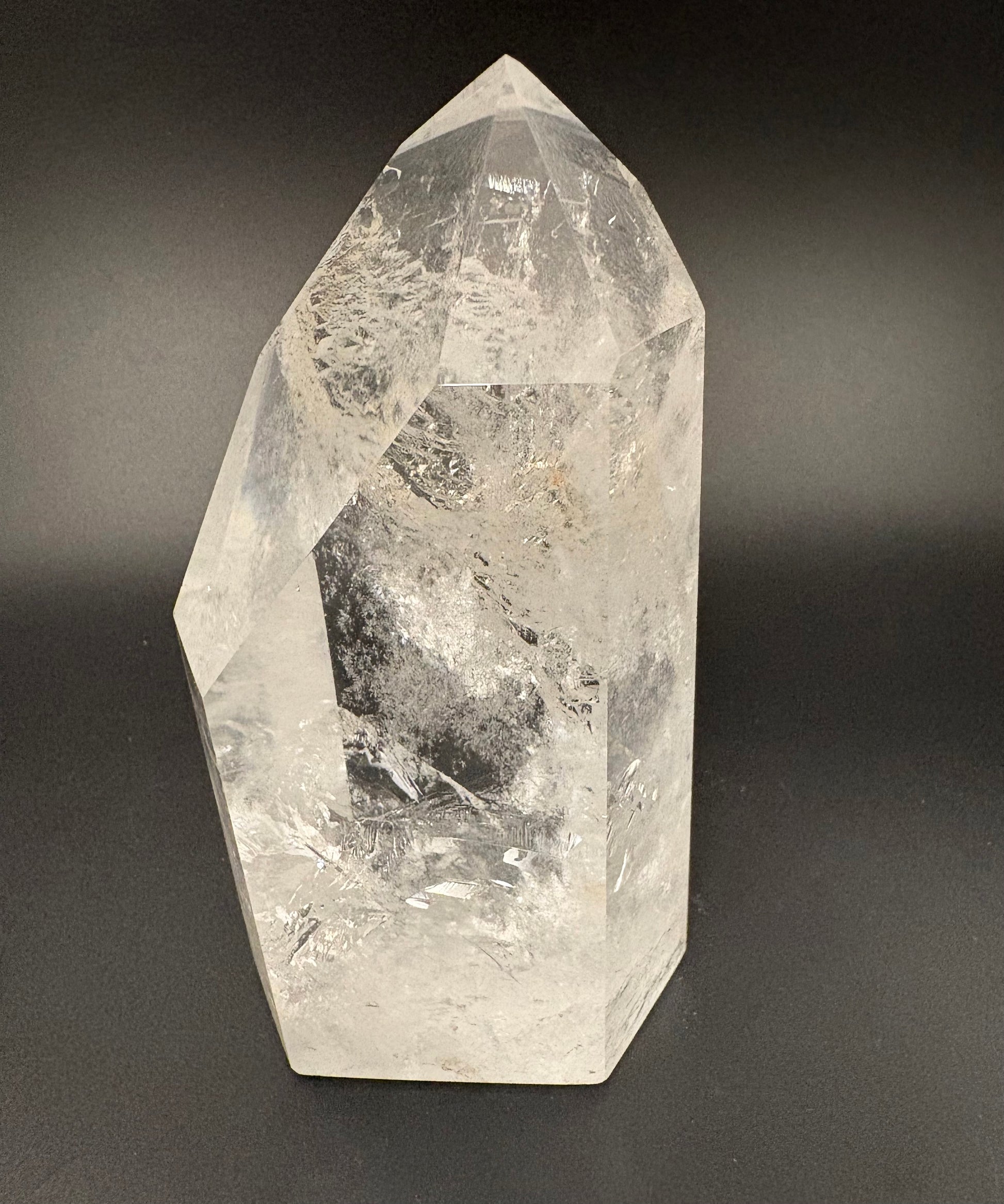 A natural clear quartz crystal point with internal inclusions, photographed against a dark gray gradient background.