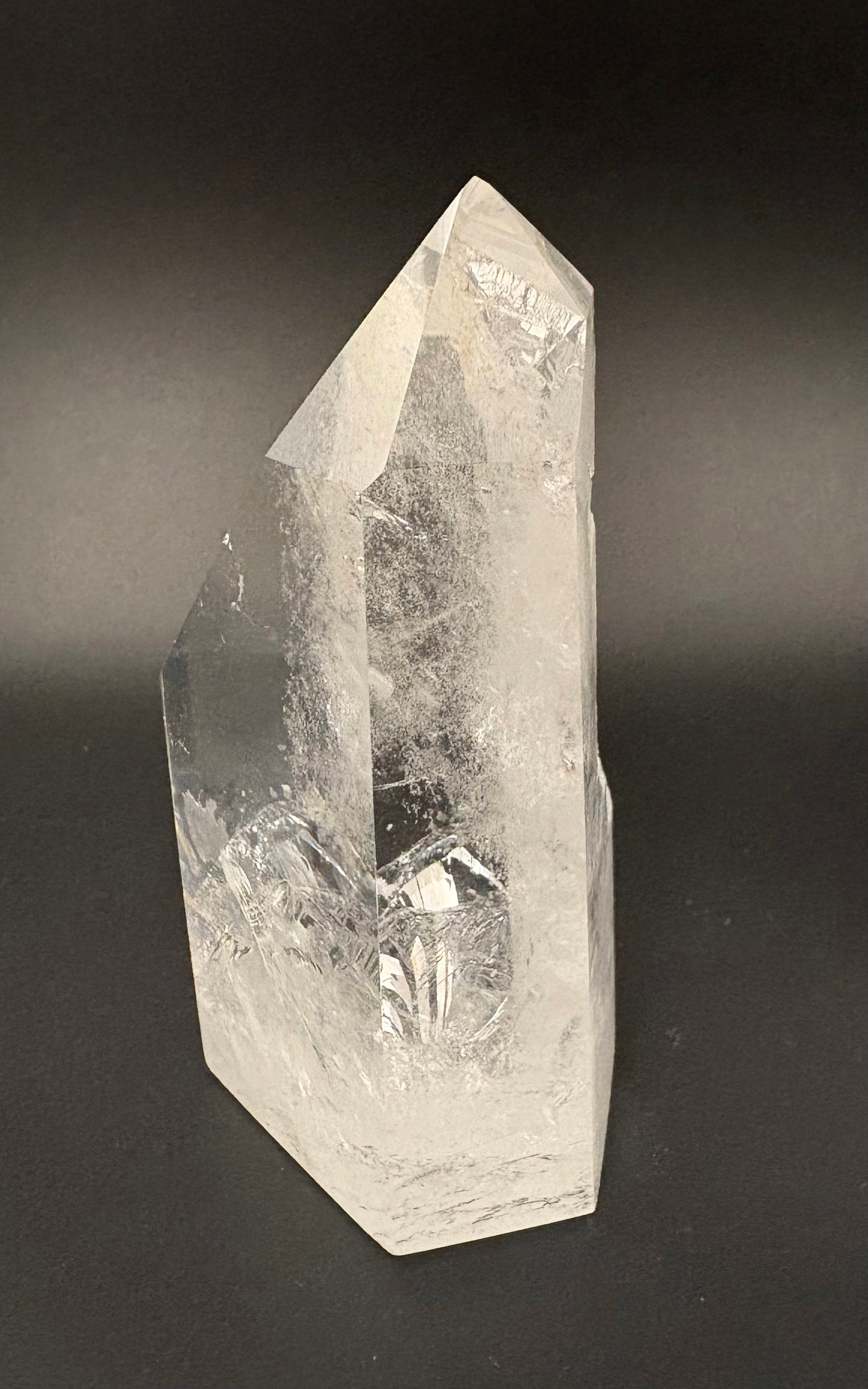 A natural clear quartz crystal point with visible internal inclusions and a faceted geometric structure, photographed against a dark gray to black gradient background.