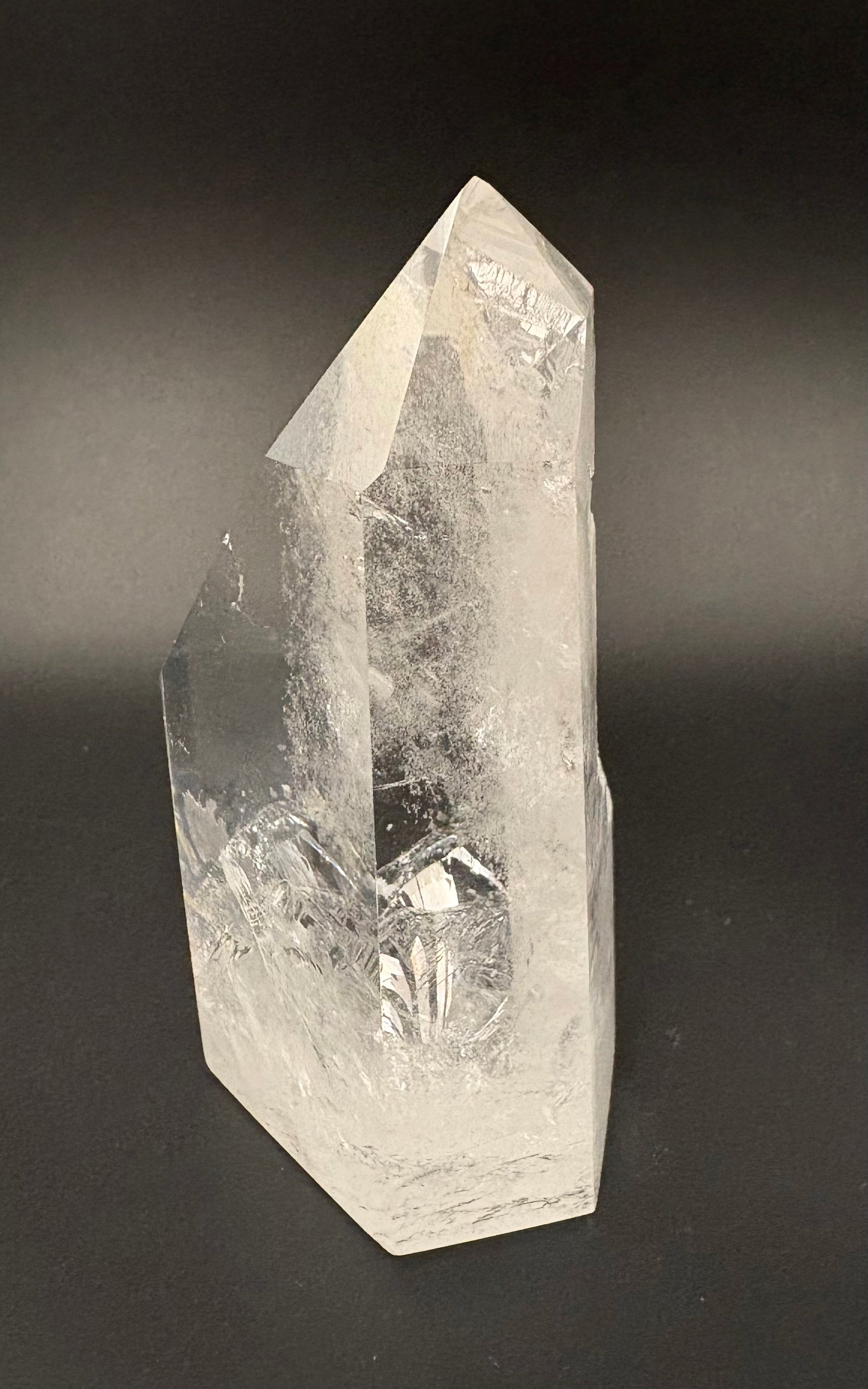 A natural clear quartz crystal point with visible internal inclusions and a faceted geometric structure, photographed against a dark gray to black gradient background.