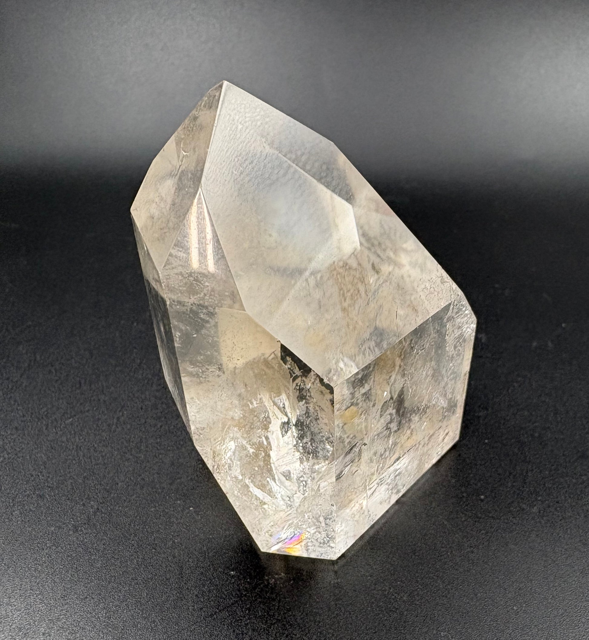 A natural clear quartz crystal tower with sharp geometric facets and internal inclusions, photographed against a dark gray gradient background.