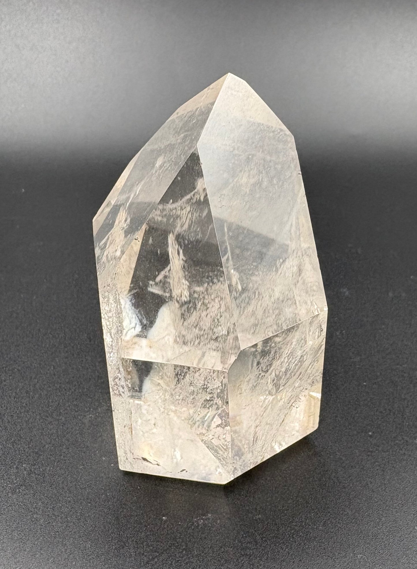 A natural clear quartz crystal tower with sharp geometric facets and internal inclusions, photographed against a dark gray gradient background.