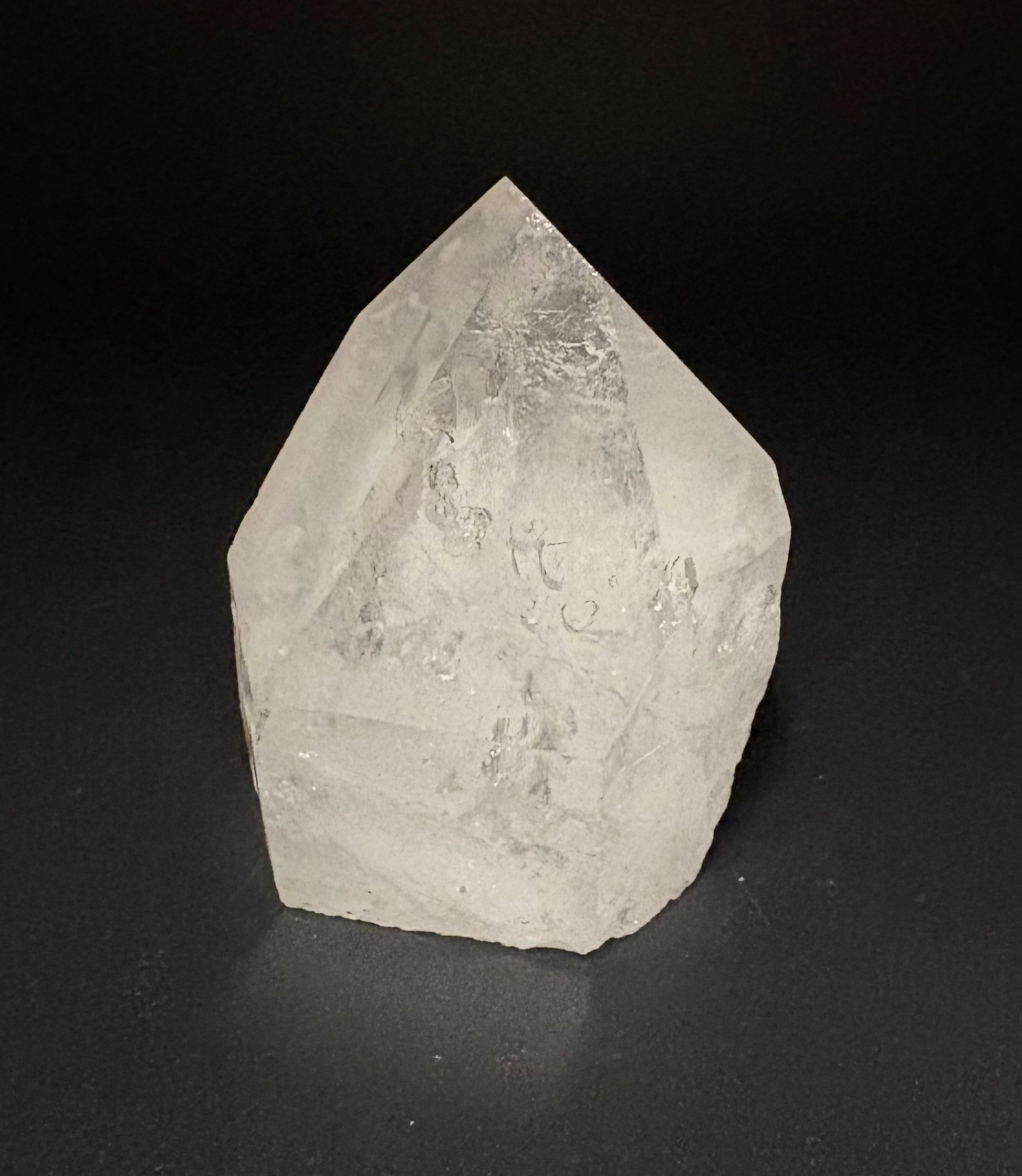 A natural clear quartz crystal point with rough, textured facets, photographed on a dark black background.