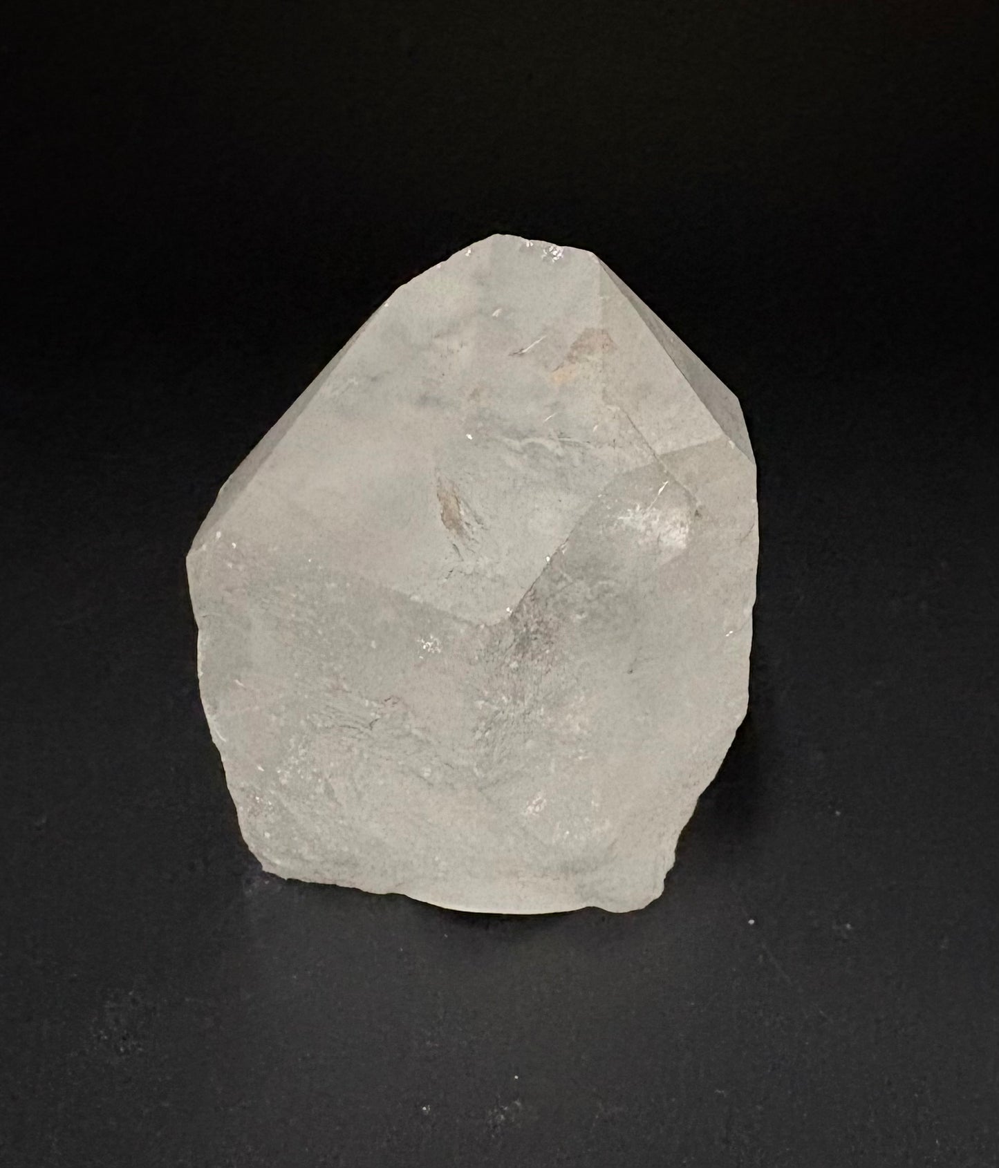 A raw, unpolished translucent crystal with a rough, faceted shape, photographed against a solid black background.