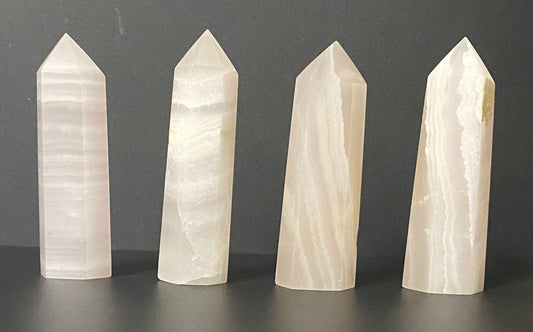Four pointed pink calcite crystal tower stakes with natural banding, displayed on a dark gray surface against a dark gray background.