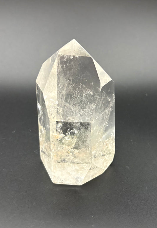 A natural clear quartz point crystal with visible internal inclusions and a hexagonal point structure, photographed on a dark gray to black gradient background.