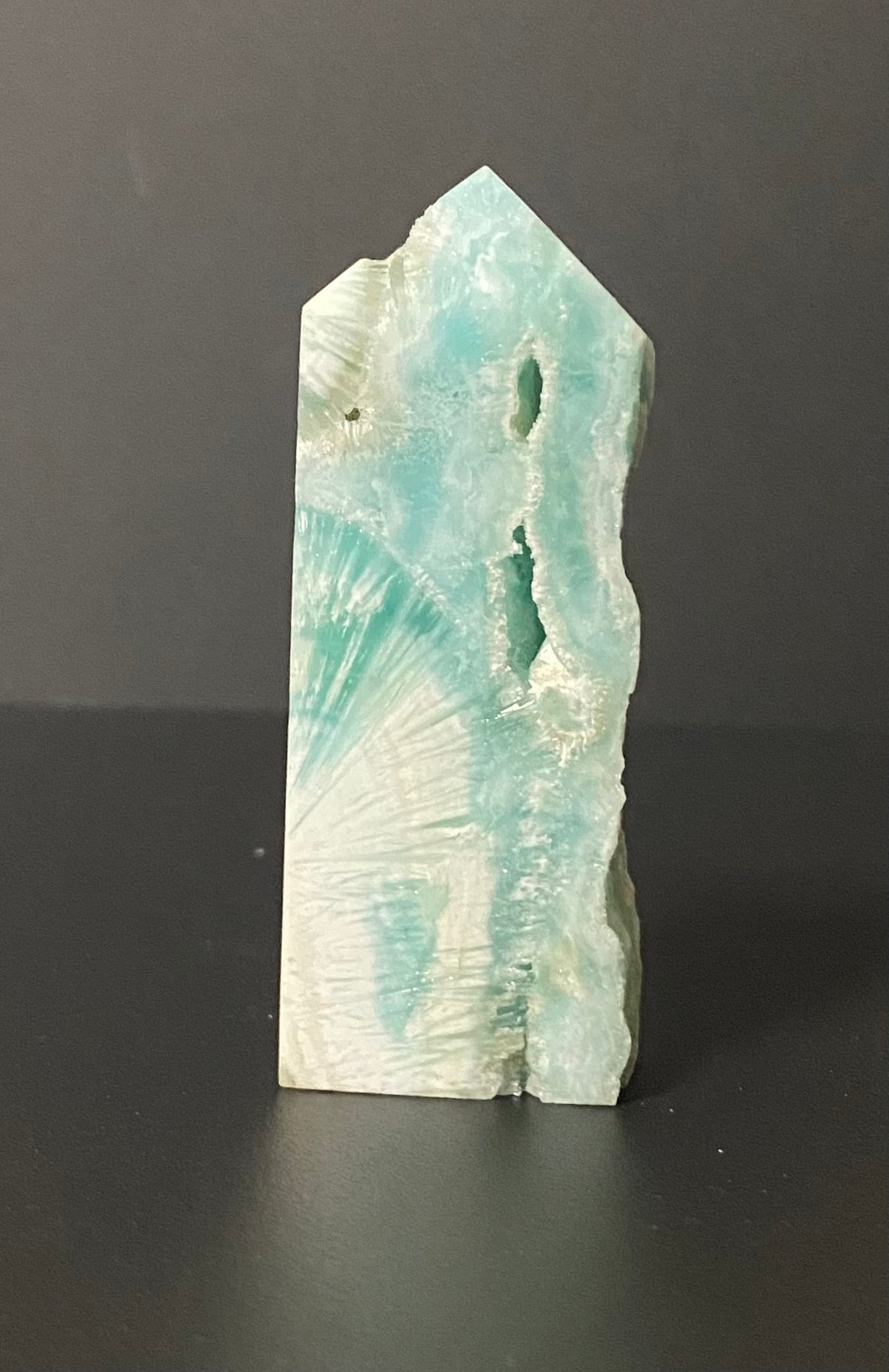 A natural mineral or crystal point specimen with a light aqua and white marbled pattern, standing upright on a dark surface against a dark gray background.