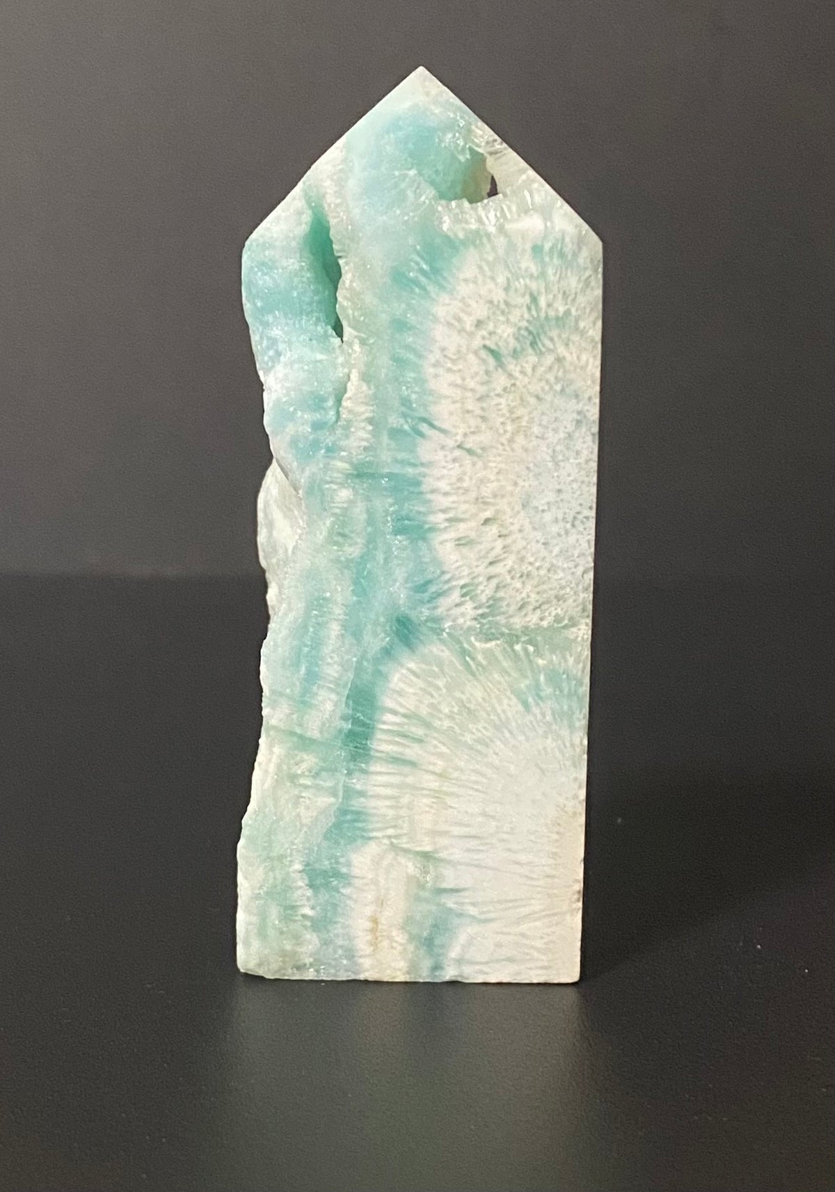 A natural pointed crystal tower Calcite, featuring a marbled pattern of light teal green and white, standing upright on a dark surface against a dark gray background.
